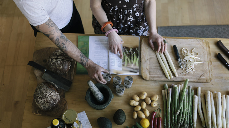 Couple reading cookbook and chopping vegetables