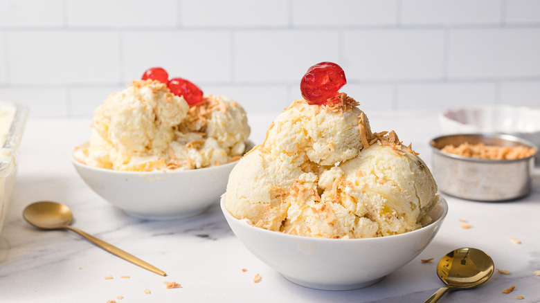 Two pineapple ice creams with maraschino cherries and spoons