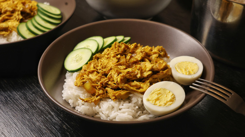 Chicken pastil over rice in a brown bowl with hard boiled egg and sliced cucumber