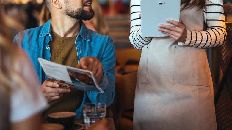 A server happily taking a guest's order as he holds a menu and points at something on it