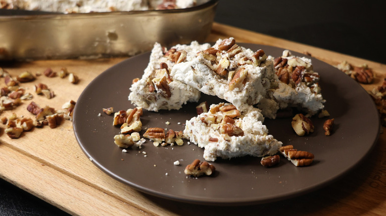 pieces of butter pecan divinity candy on a brown plate with chopped toasted pecans