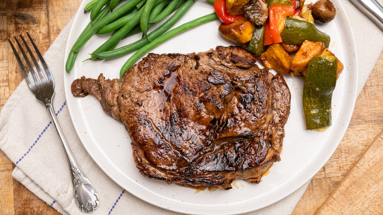 Close up of a piece of cooked marinated steak on a plate surrounded by vegetables