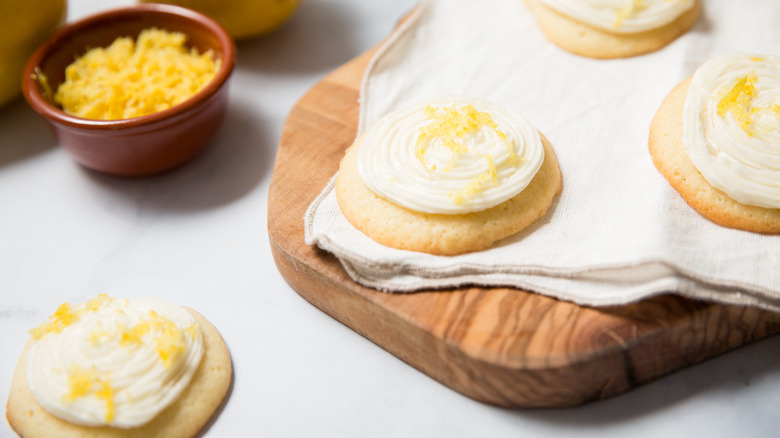 closeup of frosted lemonade cookies on table next to dish of lemon zest