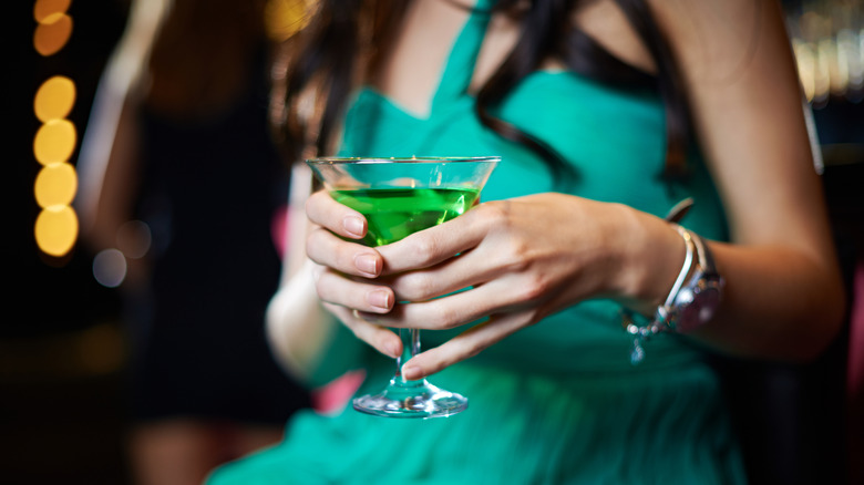 person holding a glowing green class of absinthe
