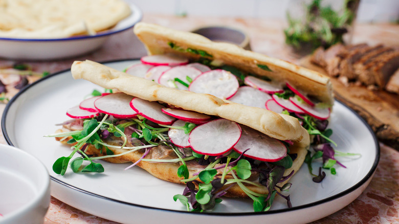 2 tuna steak sandwiches on a plate with sliced tuna steak and flatbreads in background