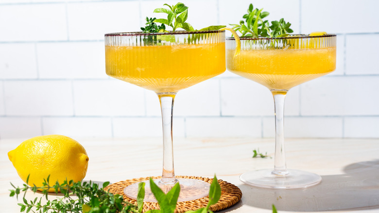 Two yellow cocktails next to lemon verbena and lemon