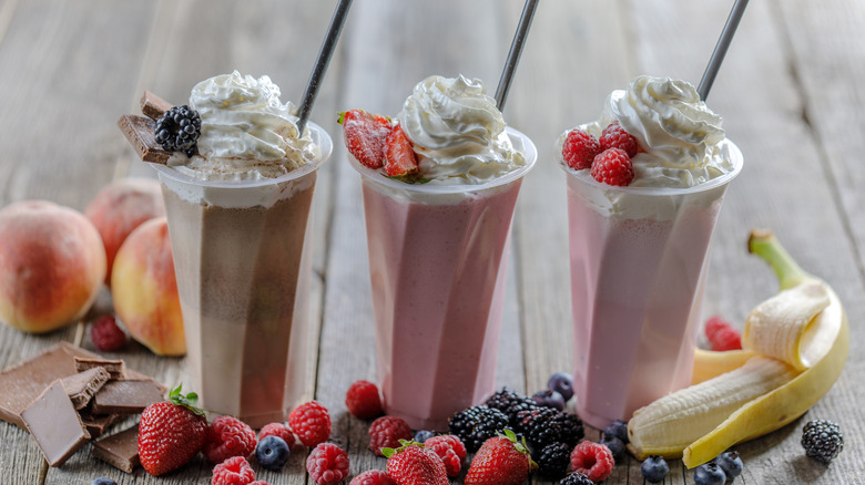 three milkshakes with whipped cream and straws with assorted fruit varieties