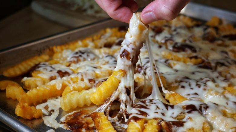 hand picking up disco fry with melted cheese strings pulling away from the rest of the pan