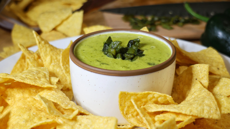 a small bowl of poblano queso dip on a plate surrounded by tortilla chips