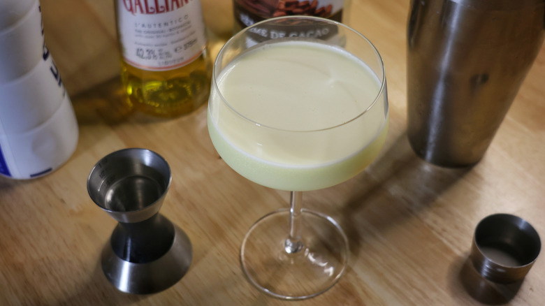 golden Cadillac cocktail on wooden table with liquor bottles and bar equipment