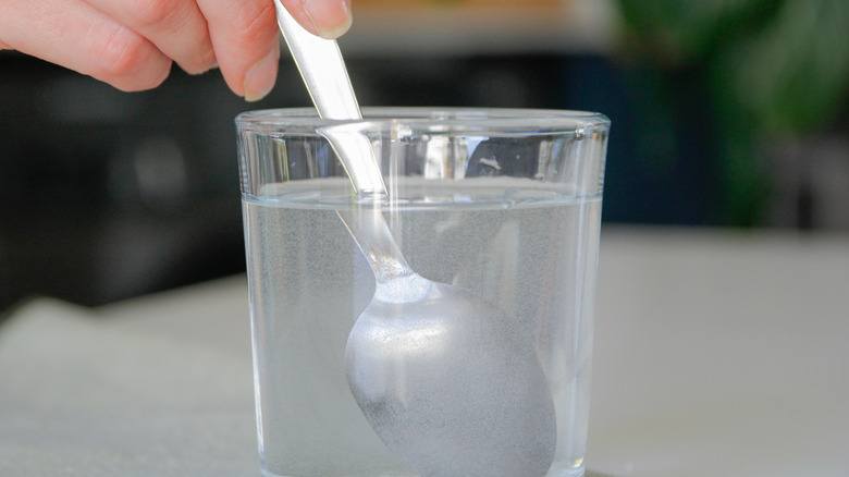 mixing powder into glass of water with silver spoon