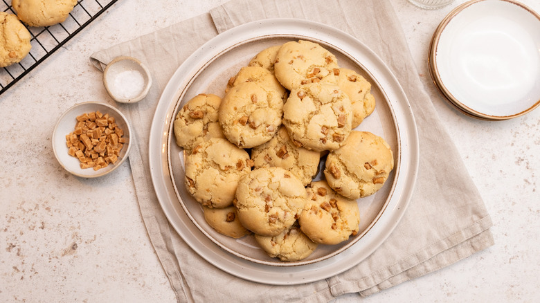 easy soft caramel cookies piled on a plate next to small bowl of caramel pieces