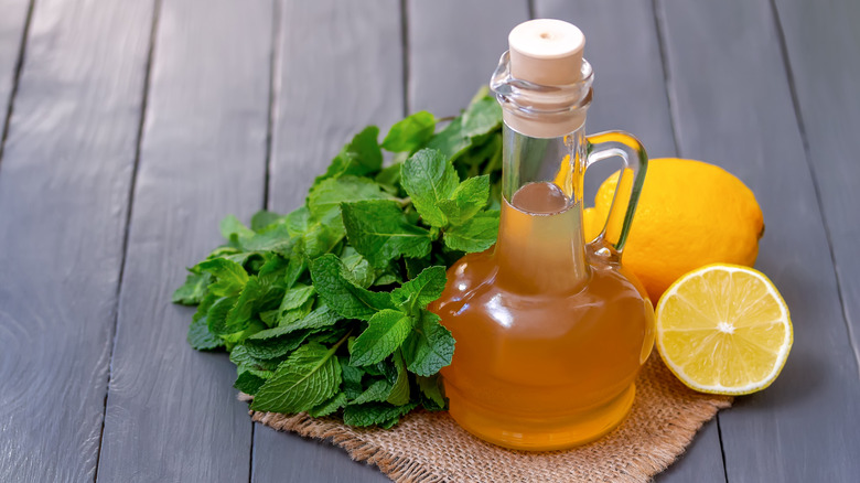 Glass bottle of golden colored simple syrup next to fresh lemons and mint leaves