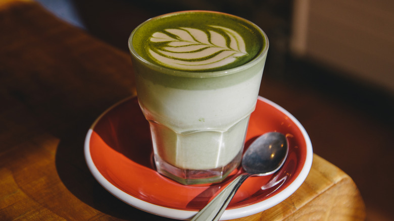 a glass of matcha latte on a saucer with a spoon