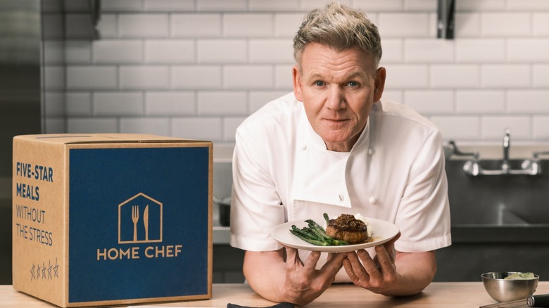 Gordon Ramsay holding a plate of food with a box of Home Chef meals next to him