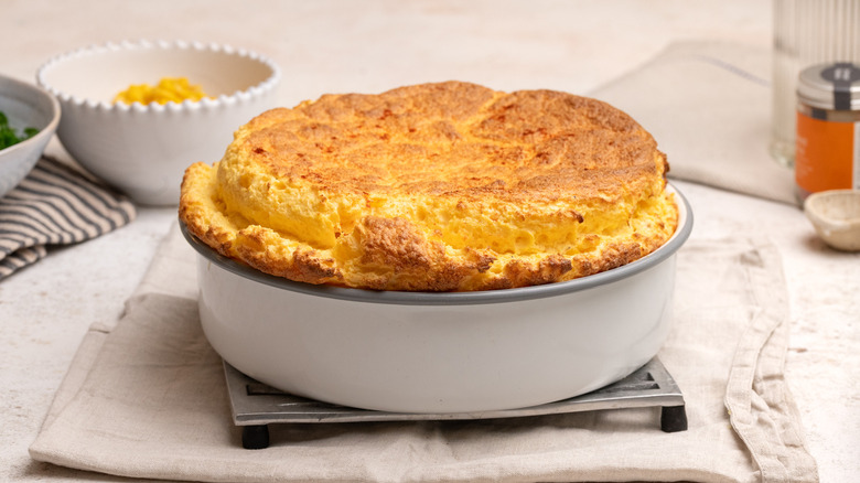 cheesy corn souffle in baking dish sitting on a trivet over a piece of cloth