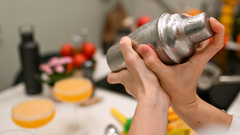 hands holding a cocktail shaker with blurry kitchen in the background