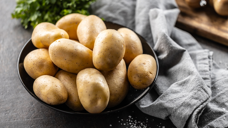 A bowl of potatoes on a table next to parsley