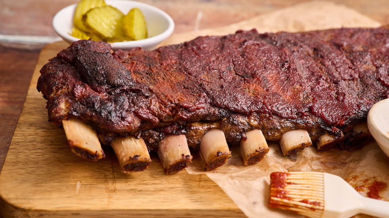 Rack of baked St. Louis-style ribs on a cutting board with basting brush in front