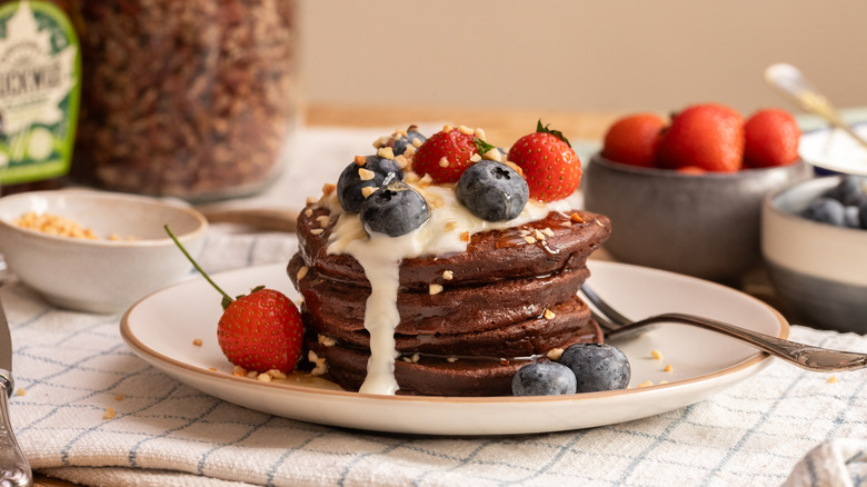 stack of high protein chocolate pancakes topped with strawberries and blueberries