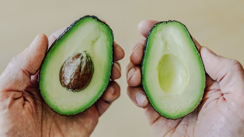 hands holding two sides of perfectly sliced avocados