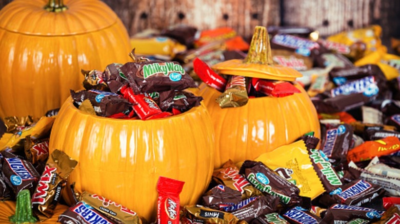 Three orange ceramic pumpkins are surrounded and filled with various mini chocolate candies in their unique branded wrappers