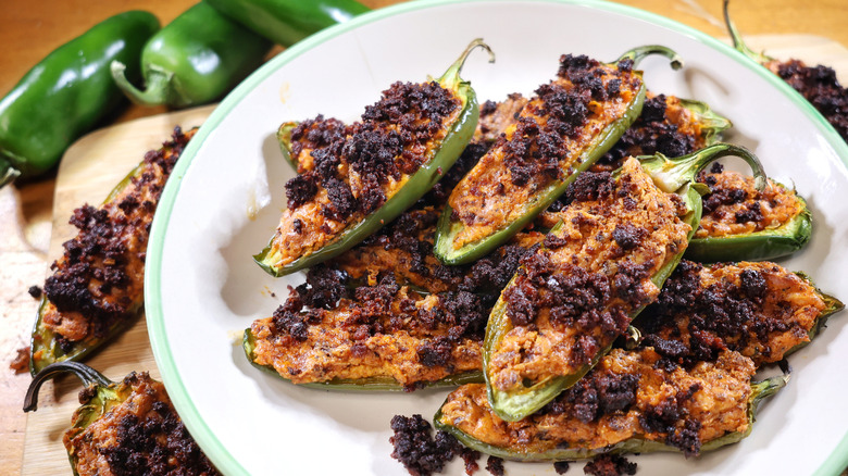 a plate of three-ingredient jalapeño poppers on a cutting board with additional jalapeño poppers and fresh jalapeños