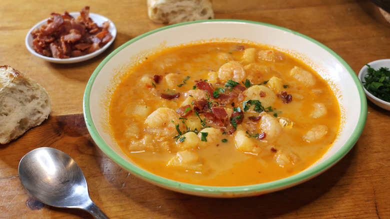 a bowl of Long Island seafood chowder on a wooden table with bread, parsley, and bacon bits