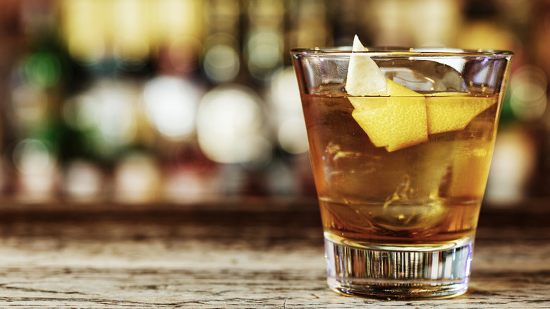 A Sazerac cocktail with a lemon garnish on a wooden bar table
