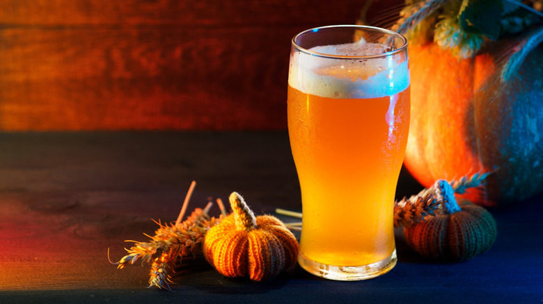 frothy glass of pumpkin beer next to small stuffed pumpkins