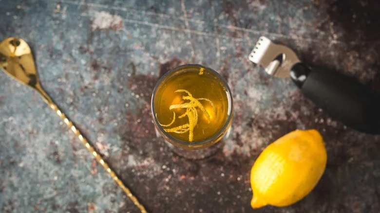 Top-down image of tequila cocktail next to lemon and bar spoon on dark surface