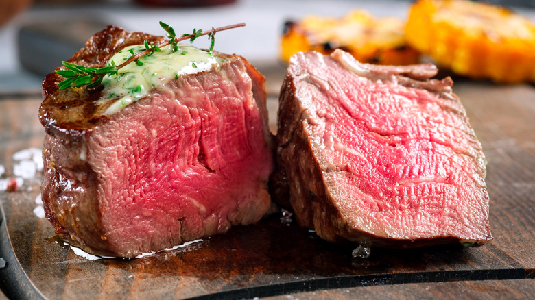 A juicy medium rare filet mignon on a plate with butter and herbs