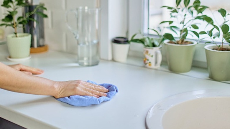 A hand using a blue cloth to clean a countertop next to a kitchen sink