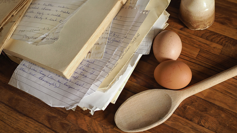 Old recipe notebook alongside two eggs and a wooden spatula