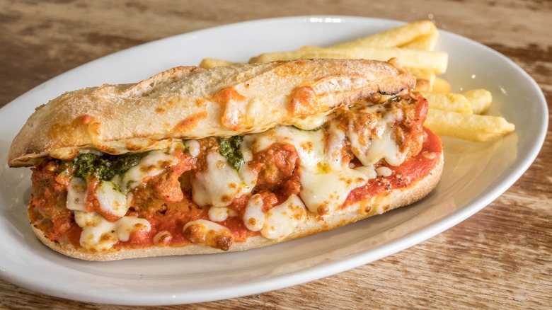 A hot sandwich full of cheese, tomato sauce, and some kind of greens on a hoagie roll