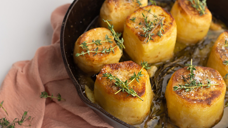 Fondant potatoes in skillet, topped with sprigs of thyme