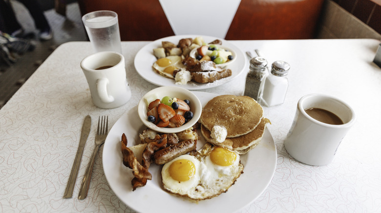 Diner meal with coffee and eggs, pancakes, bacon, and fruit on a white plate