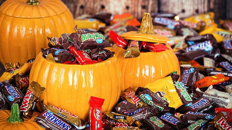 three ceramic pumpkins filled with Halloween candy, surrounded by a bunch of Halloween candy