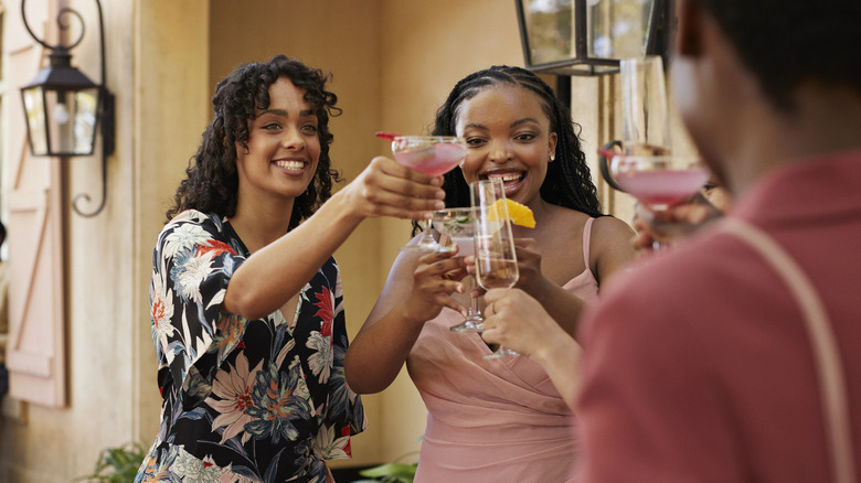 Three people standing outside toasting with cocktail glasses