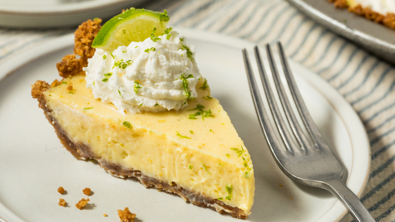 slice of key lime pie garnished with whipped cream and a lime slices on a white plate with fork