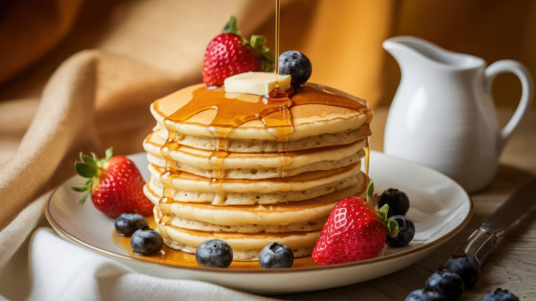 stack of pancakes with strawberries, blueberries, butter and syrup