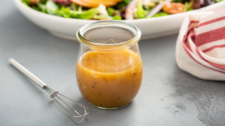 bottle of vinaigrette in front of salad bowl with whisk