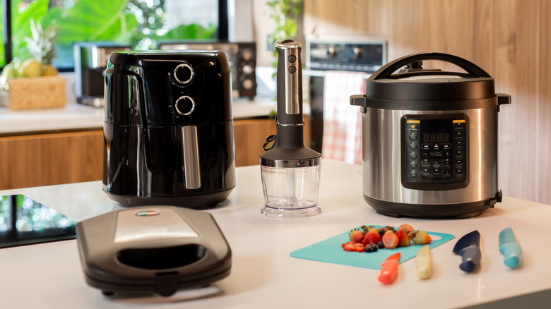 Air fryer, handheld blender, sandwich maker, and an Instant pot standing on a kitchen island