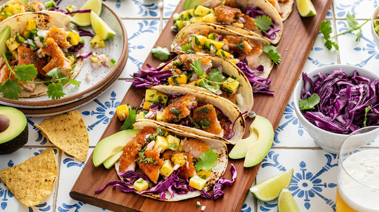 A wood board with an array of colorful fish tacos on a tile table