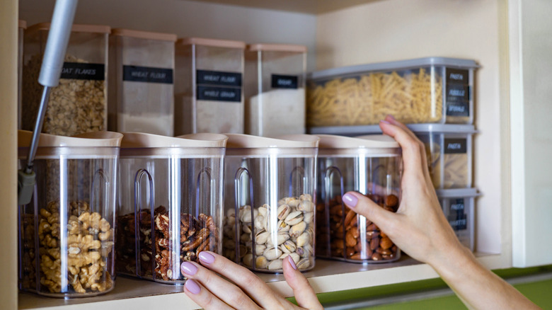 Kitchen cabinet shelf stocked with different kinds of pasta, nuts, and other essentials