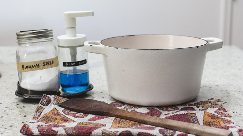 White Dutch oven with baking soda, dish soap, cloth and wooden spoon