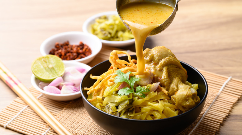 a bowl of Khao Soi soup with a ladle pouring broth into the bowl