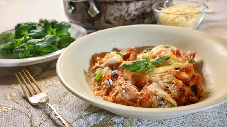 shallow bowl of baked gnocchi lasagna beside plate of fresh basil and bowl of shredded parmesan cheese