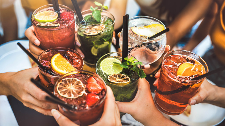 Happy people toasting cocktail glasses sitting at bar table