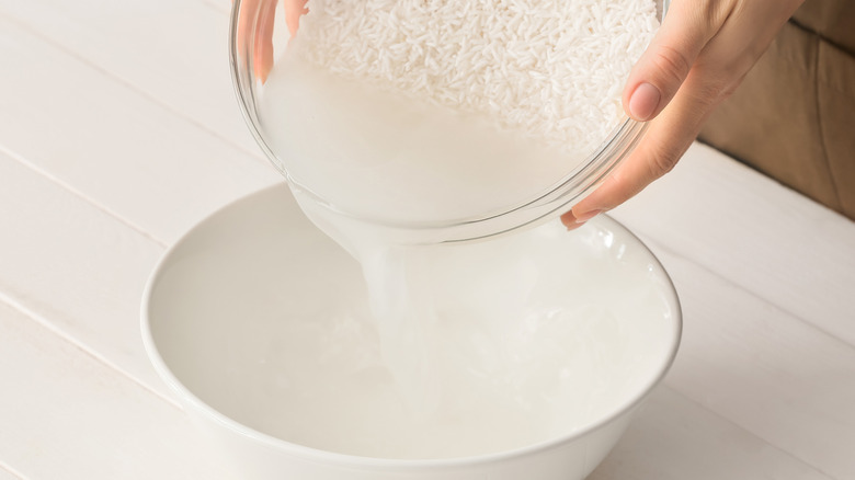 rinsing rice and pouring out the starchy rice water into a white bowl